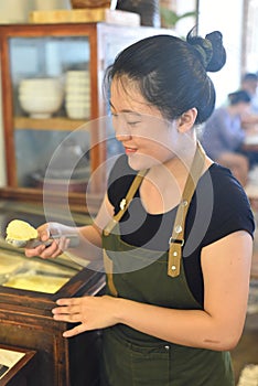Vietnamese waitress showing a scoop of homemade mango ice cream in cafe