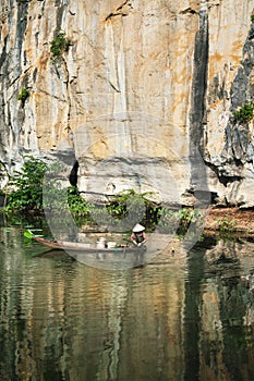 Vietnamese woman fishing for crabs on a boat along the limestone cliff in Ninh Binh, Vietnam