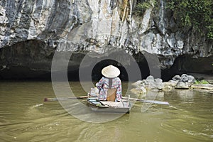 Vietnamese woman in traditional conical hat rows boat into natural cave on Ngo river, Tam Coc, Ninh Binh, Vietnam