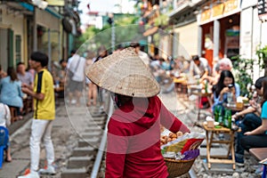 Vietnamese woman vendor walking along railroad with people drink coffee or walking on railways waiting for train to arrive on