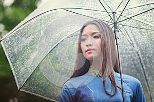 Vietnamese women wear Ao dai holding umbrella in the rain