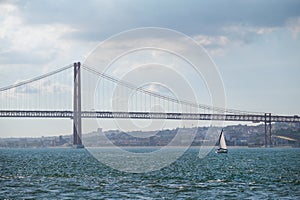 View of 25 de Abril Bridge over Tagus river with a yacht boat. Lisbon, Portugal