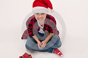 View from above of an adorable preteen boy in Santa hat, sitting on white background with christmas presents. Copy space