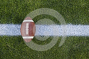 View from above of an American Football sitting on a grass football field on the yard line