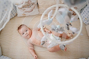 view from above. a baby lies in a white crib with mobile with toys.