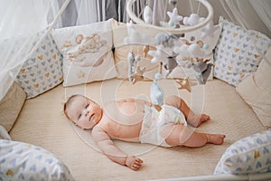 view from above. a baby lies in a white crib with mobile with toys.