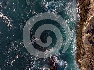 View from above. Beautiful seascape. Bubbling ocean water with white foamy waves and the edge of a rocky shore. Ecology, geology,