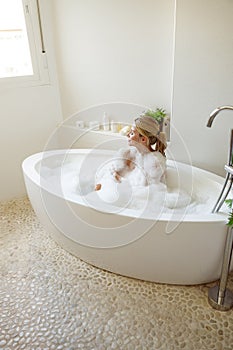 View from above on beautiful young cheerful female sitting in bathtub with bubbles foam.