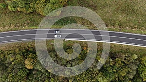 View from above. Cars are driving fast on the road in the autumn forest, car journey. Black and white car driving side