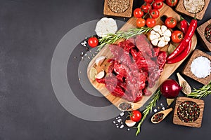 View above chopped raw beef or lamb meat with spices, seasoning, chili pepper and tomatoes over dark concrete background