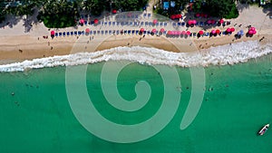 View from above of the clear sea water with tourists enjoying the beach on sun bed with red umbrella in Patong beach