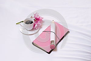 View from above. The concept of tenderness, care and love. Pink diary, a large white pencil, a cup of coffee and flowers.