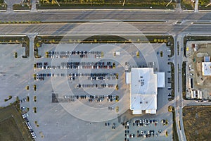 View from above of dealers outdoor parking lot with many brand new cars in stock for sale on highway side. Concept of