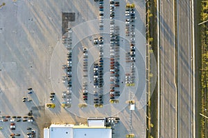 View from above of dealers outdoor parking lot with many brand new cars in stock for sale on highway side. Concept of
