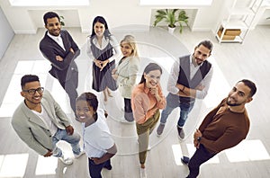 View from above of diverse team of happy young people standing in office, looking up and smiling