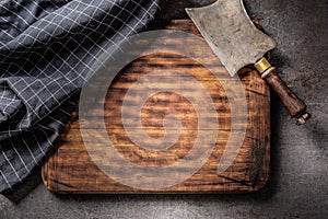 View from above on an empty cutting board, with vintage cleaver and dark checked tea towel on top of it with a dark