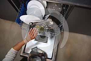 View from above of female hand loading dishes, empty out or unloading dishwasher with utensils. Kitchen appliances