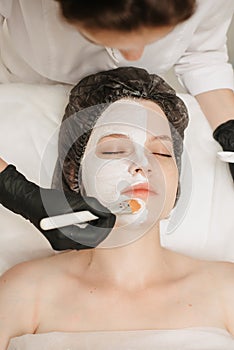 view from above of Female professional cosmetologists hands applying mask to patient& x27;s face for facial skin care.