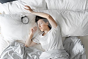 View from above. The girl sleeps next to the alarm clock. Trying to turn off the ringing alarm clock that interferes with sleep.