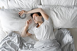 View from above. The girl sleeps next to the alarm clock. Trying to turn off the ringing alarm clock that interferes with sleep.