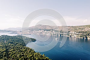 View above the green trees of a cruise ship sailing on the sea past the coast of Dubrovnik. Croatia. Drone