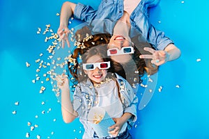 View from above happy mother and daughter laying on floor, having fun with popcorn  on blue background