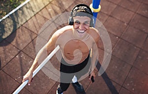 View from above of happy young male smiling after good workout outdoors. Handsome athlete man looking up with headphone listening