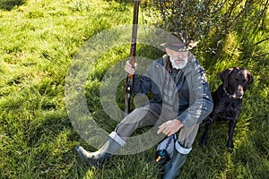 View from above on m,ature caucasian hunter sitting with dog on grass
