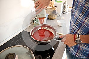 View from above of a male chef adding a fresh passata into a frying pan while cooking delicious meal in the home kitchen