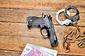 View from above of 9mm pistol - handgun, handcuffs, bullets, euro banknotes on old wooden table