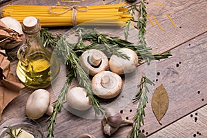 A view from above on noodles, mushrooms, oil bottle, garlic and rosemary. Uncooked ingredients on a wooden table
