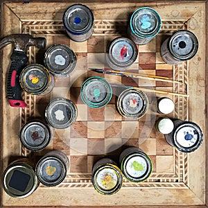 View from above of paint tins, brushes and hammer on chess board table