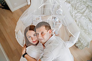 view from above. parents at a baby lies in a white crib with mobile with toys.