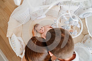 view from above. parents at a baby lies in a white crib with mobile with toys.