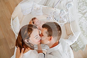 view from above. parents at a baby lies in a white crib with mobile with toys.