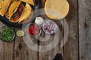 View from above of plate with hot mexican tacos on rustic wooden table with ingredients for cooking background. Concept of