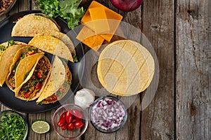 View from above of plate with mexican tacos on rustic wooden table with ingredients for cooking background. Concept of traditional