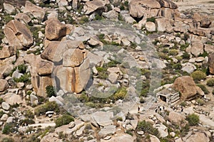 View from above of the ruins of an ancient temple in Hampi, India, with huge rocks and small tourists.