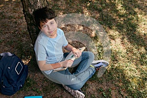 View from above of a school kid, adorable preteen boy in casual denim, reading book after school in the backyard