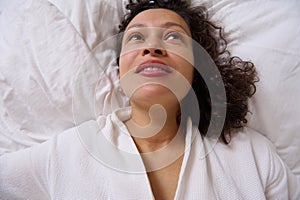 View from above smiling young adult woman waking up in the morning , lying on the bed at home bedchamber.