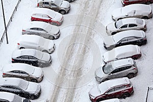 View from above at standing in lines snow covered cars in other sides of slippery road, winter parking lot near building