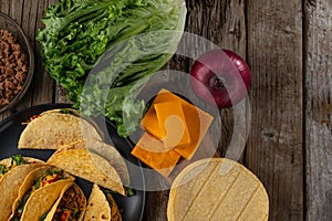 View from above of tasty mexican tacos on rustic wooden table with ingredients for cooking background. Concept of traditional meal