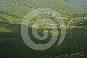 View from above of a tent camp among green alpine meadows.