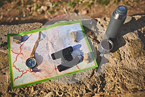 View from above of tourist's clothes, map, compass, binoculars and thermos flask lying down on the rock. Still life