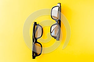 View from above of two pairs 3D black glasses on yellow background