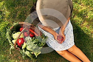 View from above of a young female gardener sitting on the grass with a basket with freshly picked ecological vegetables at the