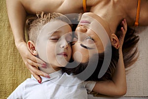 View from above of young positive family mother and son laughing and hugging while lying on bed