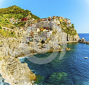 A view across the rocky coastline towards the village of Manarola, Cinque Terre, Italy
