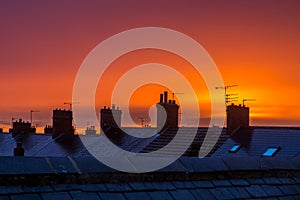 A view across roofs at sunset with chimneypots silhouetted against a vibrant sky