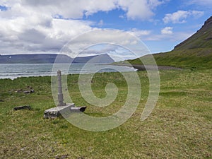 View on adalvik cove with rusty water pump and summer cottages at latrar in west fjords nature reserve Hornstrandir in photo